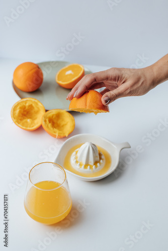 a woman's hand squeezes juice from an orange on a manual juicer, next to a plate with halves of oranges, white background