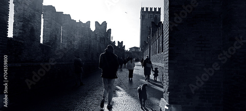 Enigmatic Noir  Silhouettes wander near an ancient castle  shadows dance in contrast to sunlight  creating a mysterious and captivating black-and-white scene