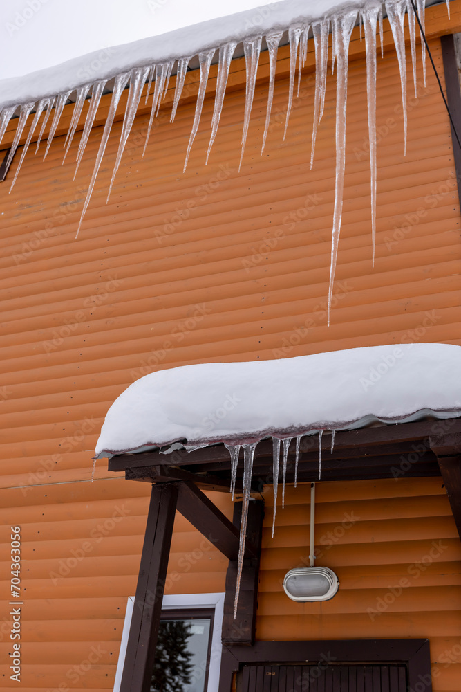 Huge icicles hang from the roof of a building with an orange facade Huge icicles hang from the roof of a building with an orange facade
