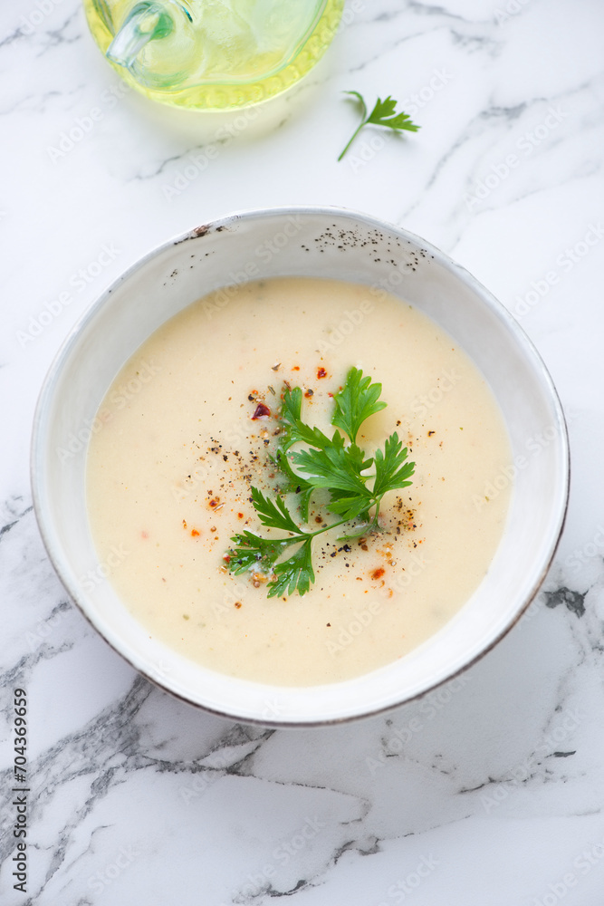 Bowl of cheese soup with fresh parsley on a white marble background, vertical shot, high angle view Bowl of cheese soup with fresh parsley on a white marble background, vertical shot, high angle view