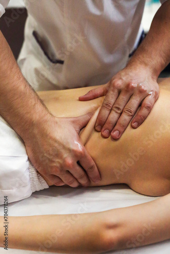 Crop masseuse massaging back of woman in salon