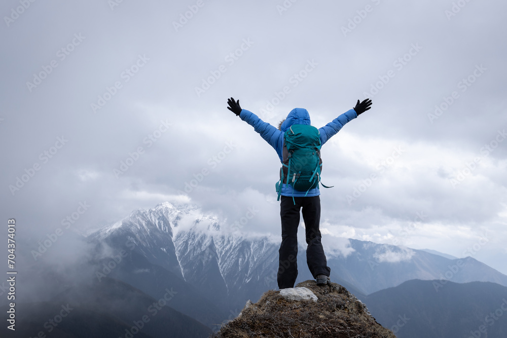Woman hiker enjoy the view on mountain top cliff edge face the snow capped mountains in tibet Woman hiker enjoy the view on mountain top cliff edge face the snow capped mountains in tibet