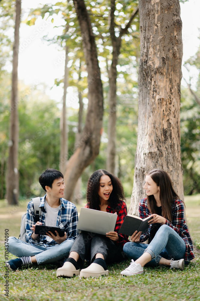 Three young college students is reading a book while relaxing sitting on grass in a campus park with her friends. Education concept