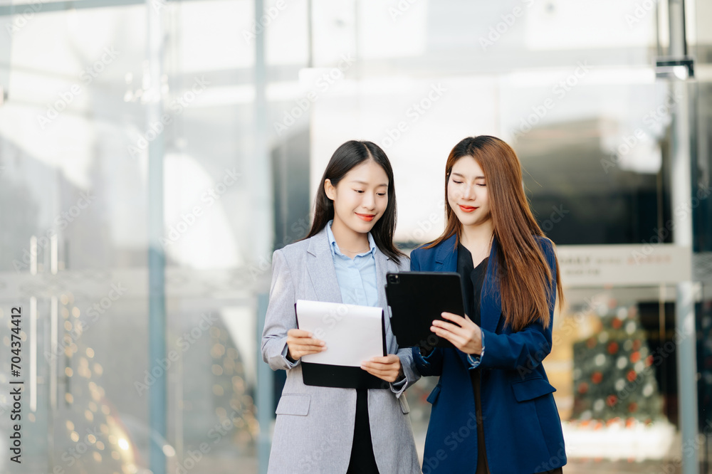 Businesswoman and woman going in city center in smart casual business style, talking, working together, stylish freelance people, holding tablet Businesswoman and woman going in city center in smart casual business style, talking, working together, stylish freelance people, holding tablet
