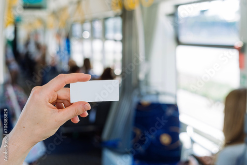 Selective focus on passenger hand holding ticket against blurred public transport interior photo