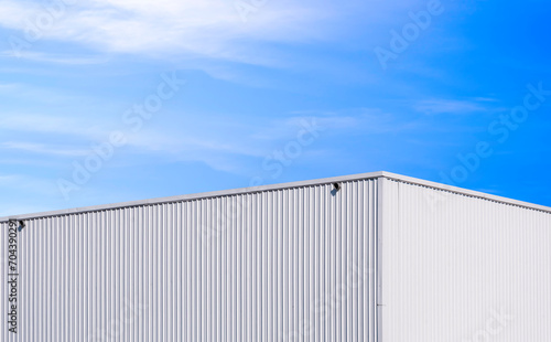Modern white metal industrial warehouse building against blue sky background, perspective side view 