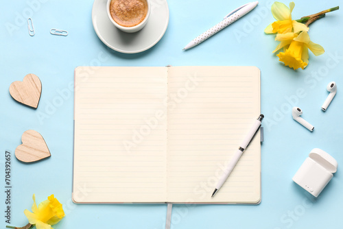 Composition with notebook, cup of coffee, earphones and beautiful narcissus flowers on blue background