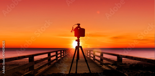 Fotokamera mit Stativ vor einem Sonnenuntergang am Meer