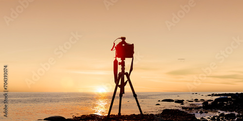 Fotokamera mit Stativ vor einem Sonnenuntergang am Meer