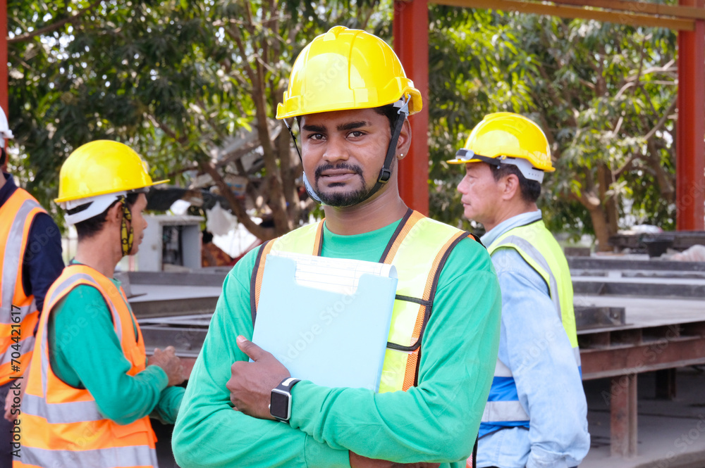 Worker wearing safety helmet stands smiling at construction site. Worker wearing safety helmet stands smiling at construction site.
