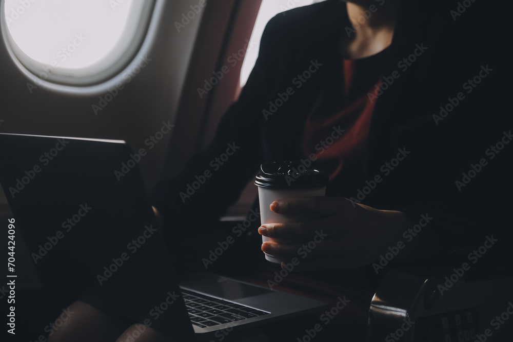Blonde female tourist checking incoming notification on smartphone sitting on seat of airplane with netbook.Young businesswoman share media from telephone on laptop computer during plane flight