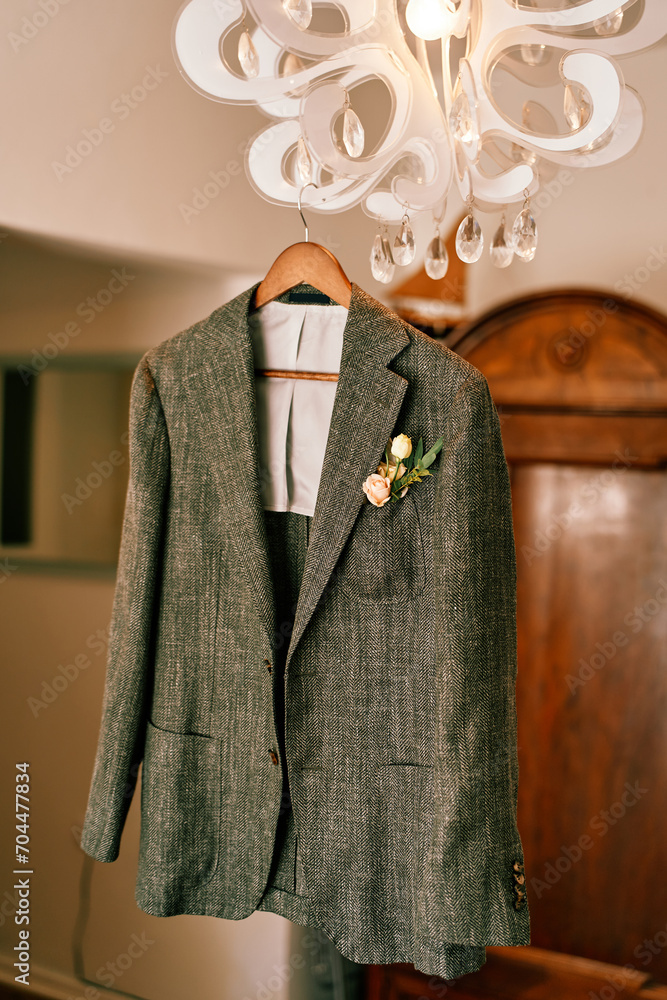 Groom gray jacket hangs on a chandelier in a hotel room