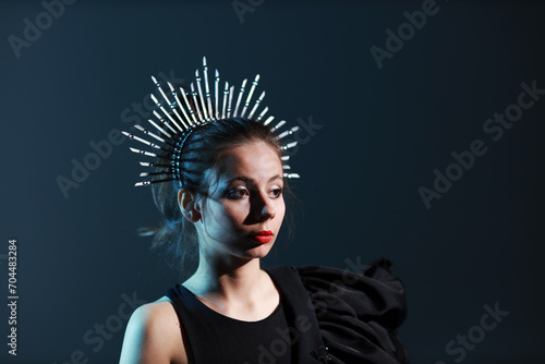 Studio portrait of beautiful young brunette woman in black dress with a crown on her head