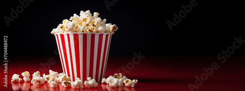 Delicious popcorn in a red striped carton box on a dark red background with copy space