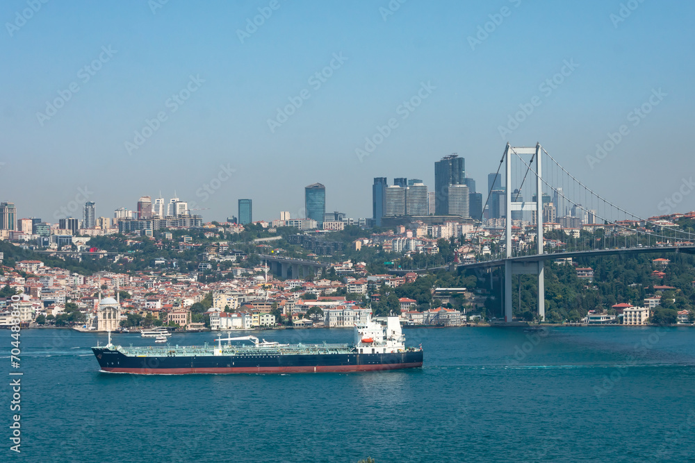 Cargo ship sails along the Bosphorus Strait under a bridge with the city and skyscrapers of Istanbul in the background