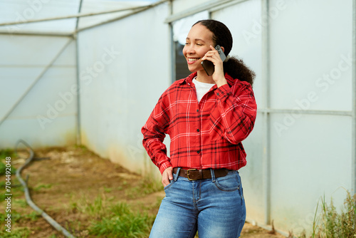 Multi-ethnic female farmer standing in greenhouse talking on the phone, smiling. photo