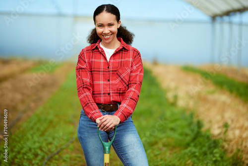 Multi-ethnic female farmer standing in a greenhouse, holding spade, smiling. photo