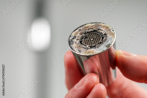 Photography A plumber is holding a chrome faucet aerator with lime scale in kitchen