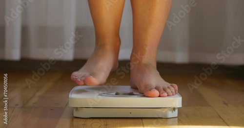 A woman measures her weight on white scale on floor, measuring tape falls off photo