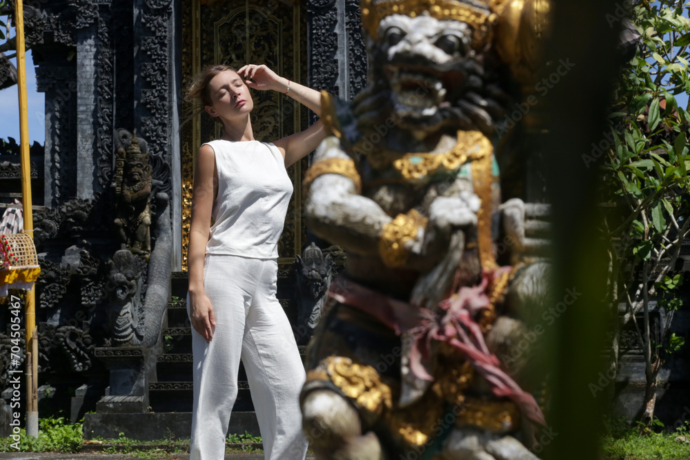 Caucasian tourist woman in white linen outfit posing in front of Hindu temple in Bali, Indonesia