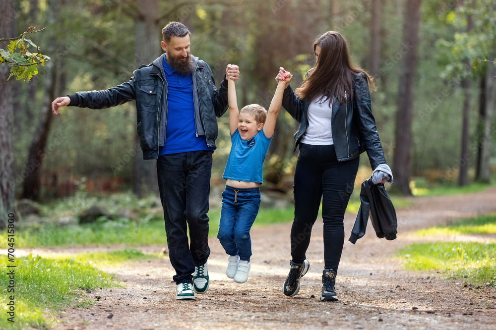 Happy family, father and mother lift their cheerful son by the arms during a walk in the forest Happy family, father and mother lift their cheerful son by the arms during a walk in the forest