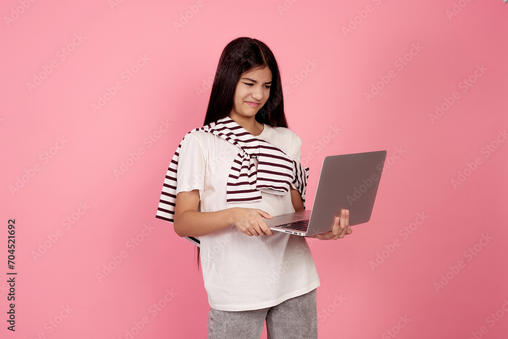 Young upset teenage girl and laptop on pink background in studio. Young upset teenage girl and laptop on pink background in studio.