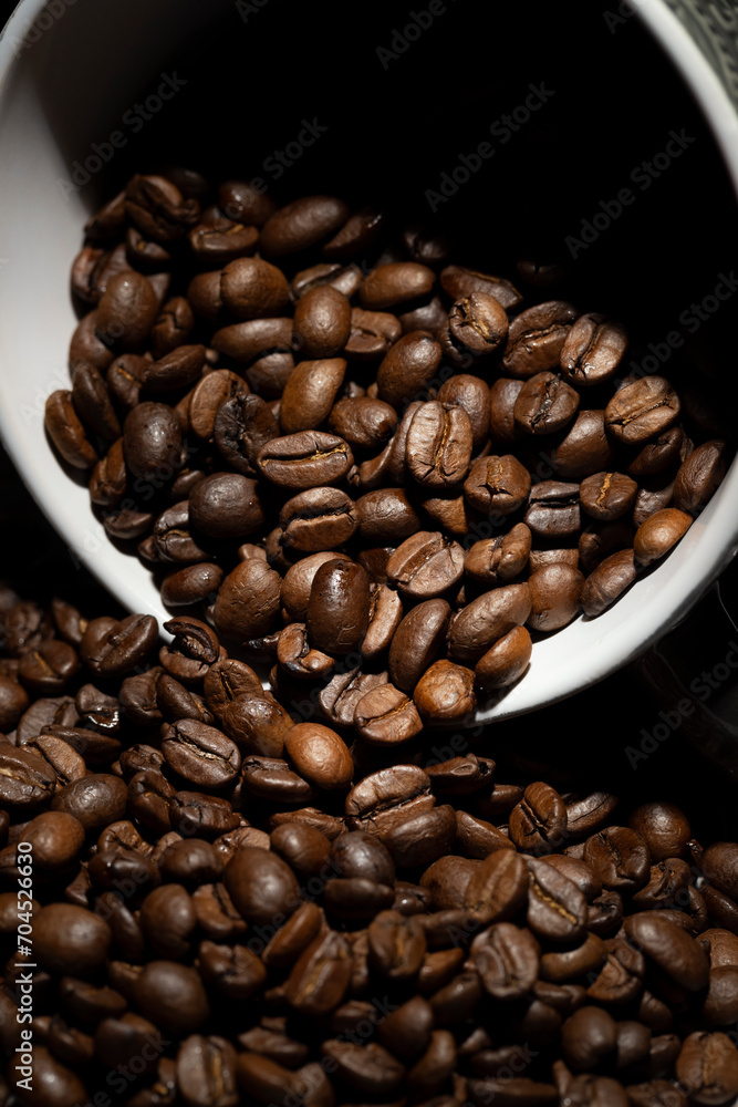 Fototapeta premium Large roasted coffee beans poured from a ceramic cup onto the table