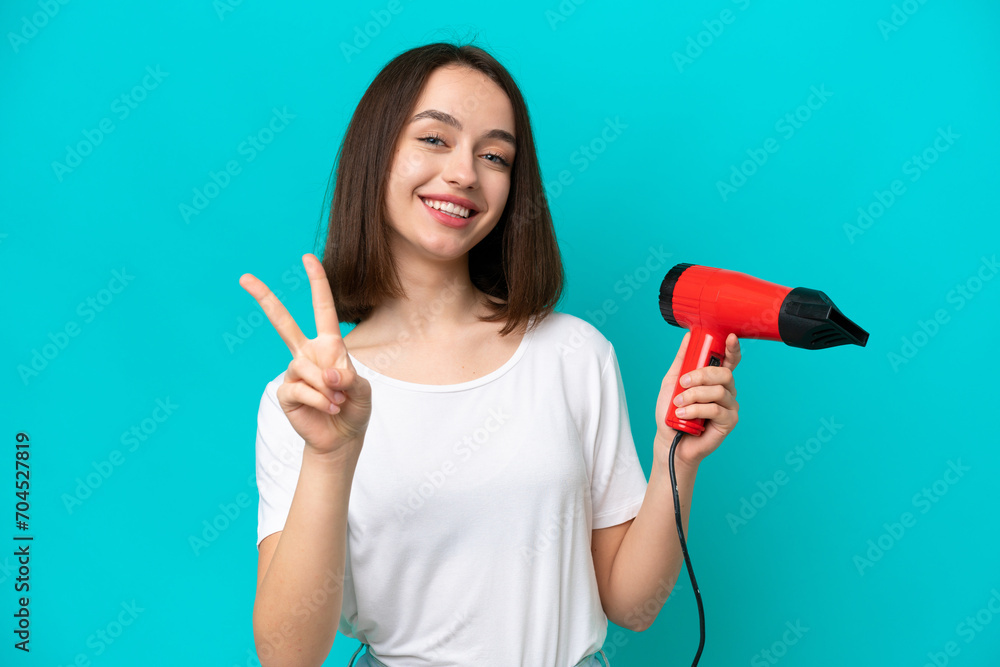Young Ukrainian holding a hairdryer isolated on blue background smiling and showing victory sign Young Ukrainian holding a hairdryer isolated on blue background smiling and showing victory sign