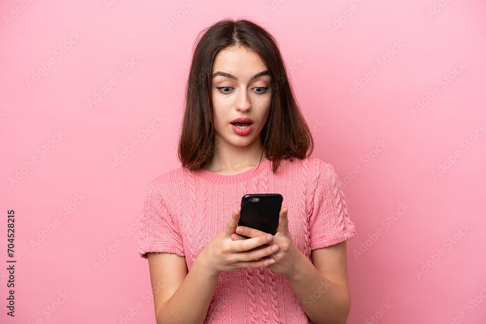 Young Ukrainian woman isolated on pink background looking at the camera while using the mobile with surprised expression Young Ukrainian woman isolated on pink background looking at the camera while using the mobile with surprised expression