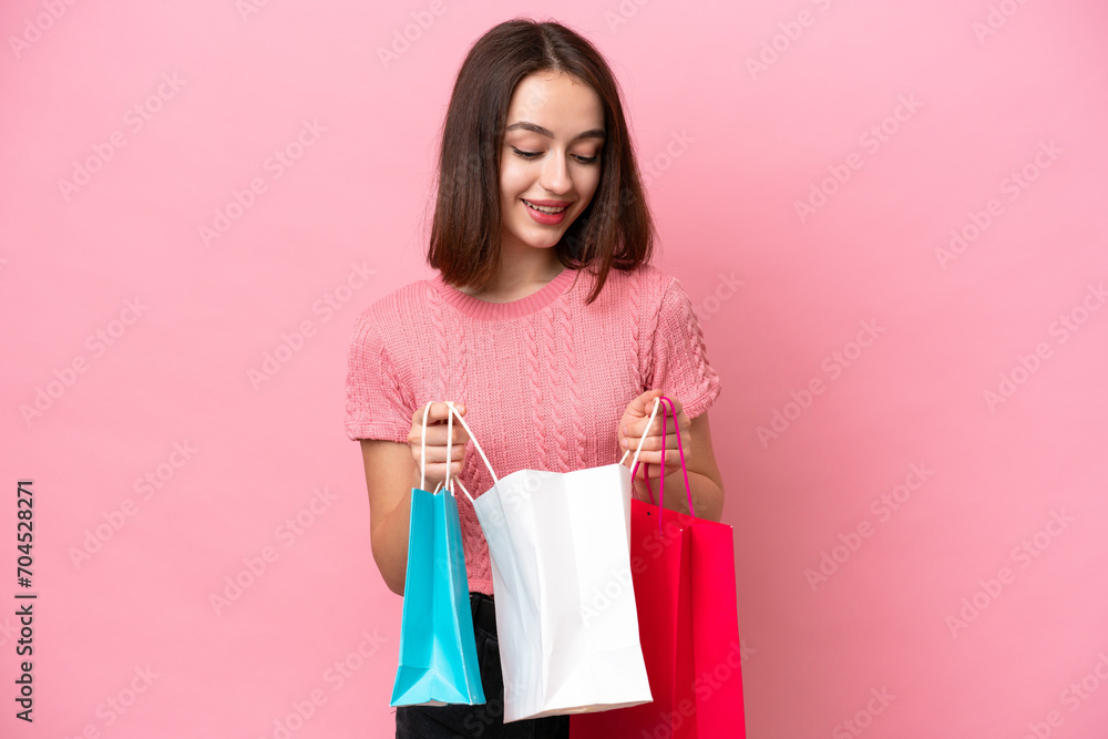 Young Ukrainian woman isolated on pink background holding shopping bags and looking inside it