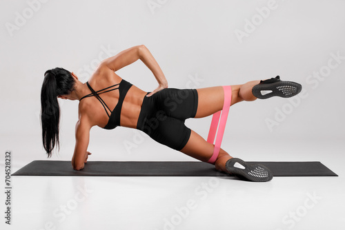 Obraz na plátne Fitness woman doing clamshell exercise for glutes with resistance band on gray background