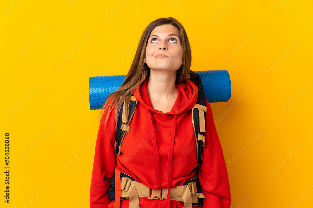 Slovak mountaineer woman with a big backpack isolated on yellow background and looking up Slovak mountaineer woman with a big backpack isolated on yellow background and looking up