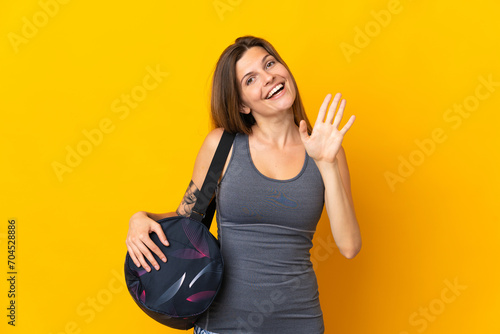 Slovak sport woman with sport bag isolated on yellow background saluting with hand with happy expression