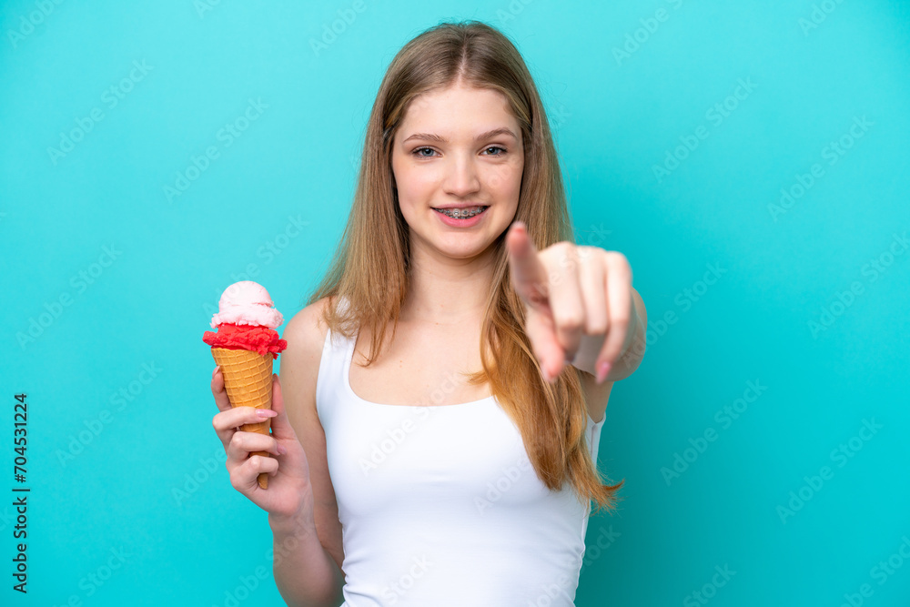 Teenager Russian girl with a cornet ice cream isolated on blue background points finger at you with a confident expression Teenager Russian girl with a cornet ice cream isolated on blue background points finger at you with a confident expression