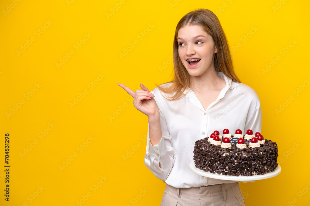 Teenager Russian girl holding birthday cake isolated on yellow background intending to realizes the solution while lifting a finger up Teenager Russian girl holding birthday cake isolated on yellow background intending to realizes the solution while lifting a finger up