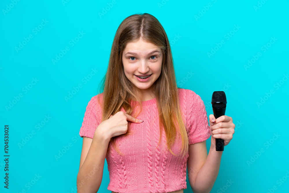 Singer Russian girl picking up a microphone isolated on blue background with surprise facial expression Singer Russian girl picking up a microphone isolated on blue background with surprise facial expression