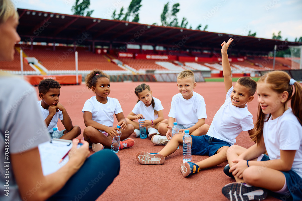 Fototapeta premium Happy boy raising his hand to ask question during sports training at athletics club.