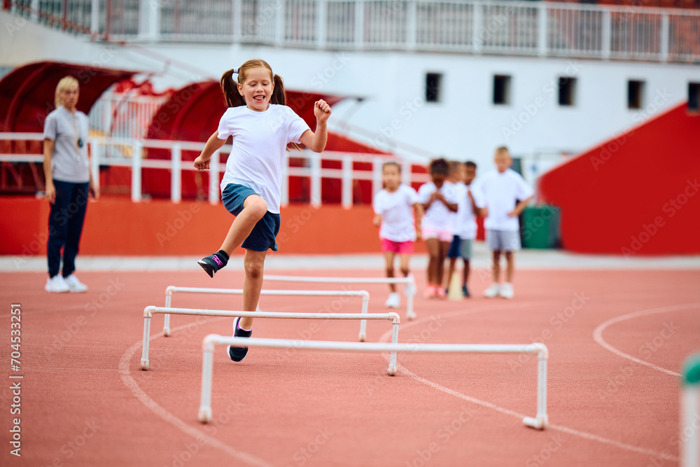Obraz premium Happy girl jumping over obstacles while running at stadium.