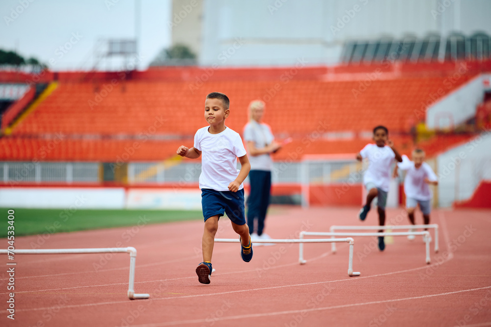 Obraz premium Little boy jumping over obstacles while running on track at athletics club.