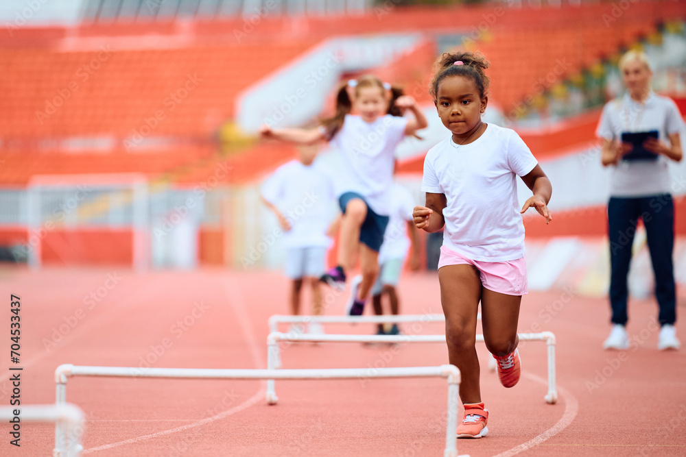 Black little girl running on track during sports training at stadium.