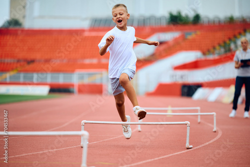 Cheerful kid umping over obstacles while running during sports training at stadium.