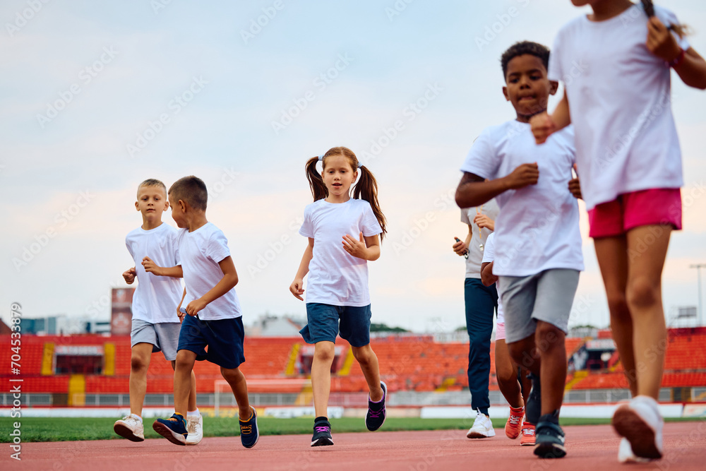 Little girl and her friends running during sports training at athletics club.