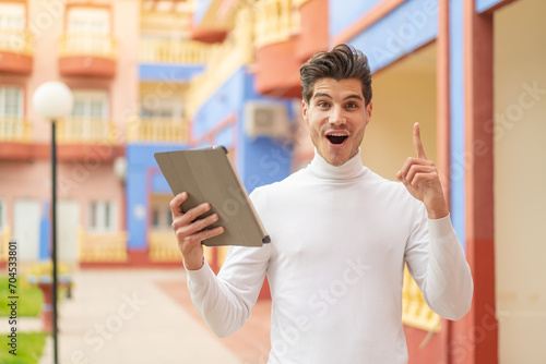 Young caucasian man holding a tablet at outdoors pointing up a great idea