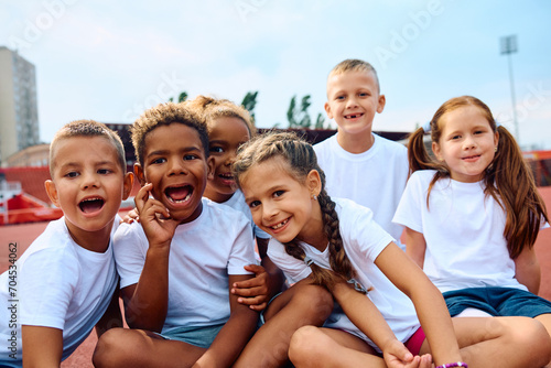 Multiracial group of cheerful kids during exercise class at stadium looking at camera. photo