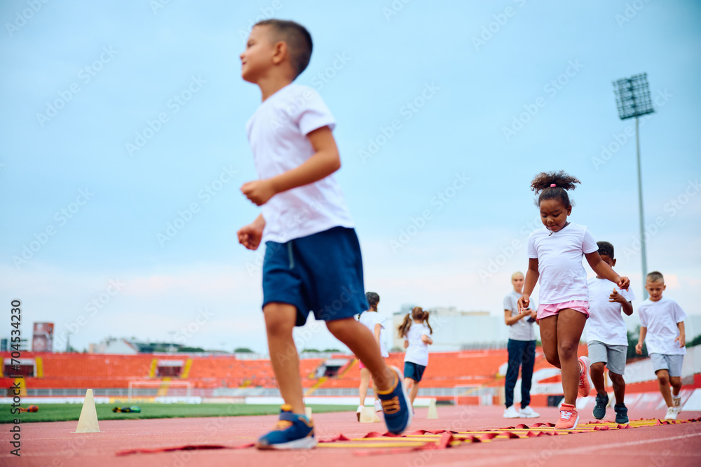 Black girl crossing agility ladder during PE class at stadium.