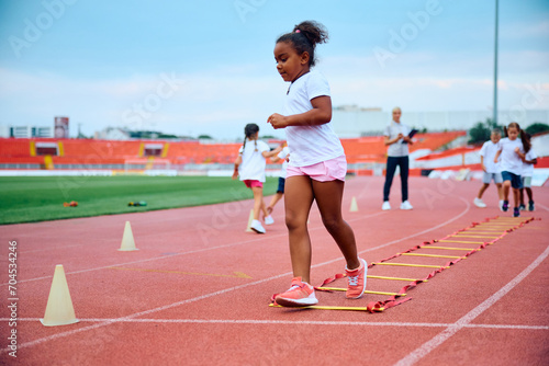 African American little girl running during exercise class at stadium.