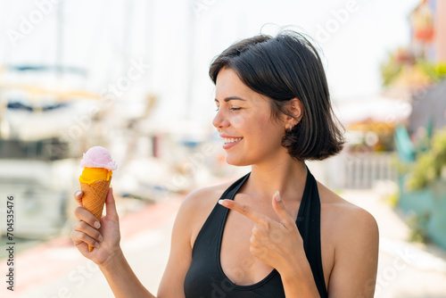 Young pretty Bulgarian woman with a cornet ice cream at outdoors and pointing it