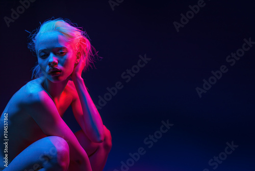 Nude young blonde woman in theatre pink spotlight, copy space on dark blue background photo
