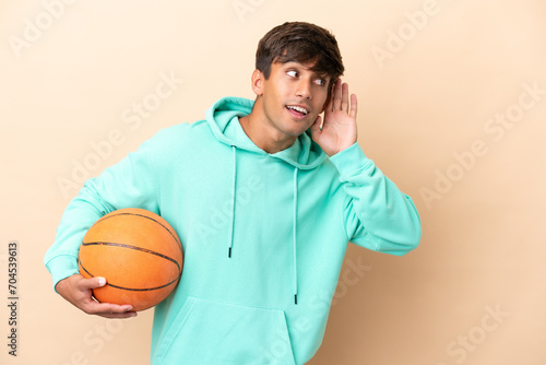Handsome young basketball player man isolated on ocher background listening to something by putting hand on the ear