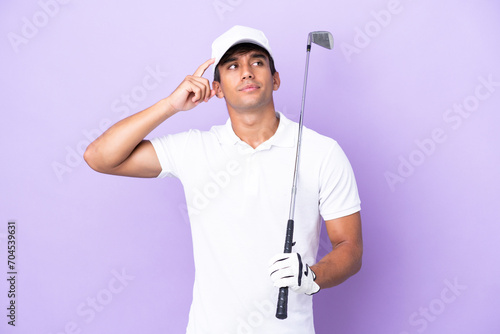 Young caucasian man isolated on purple background playing golf and and having doubts confuse face expression